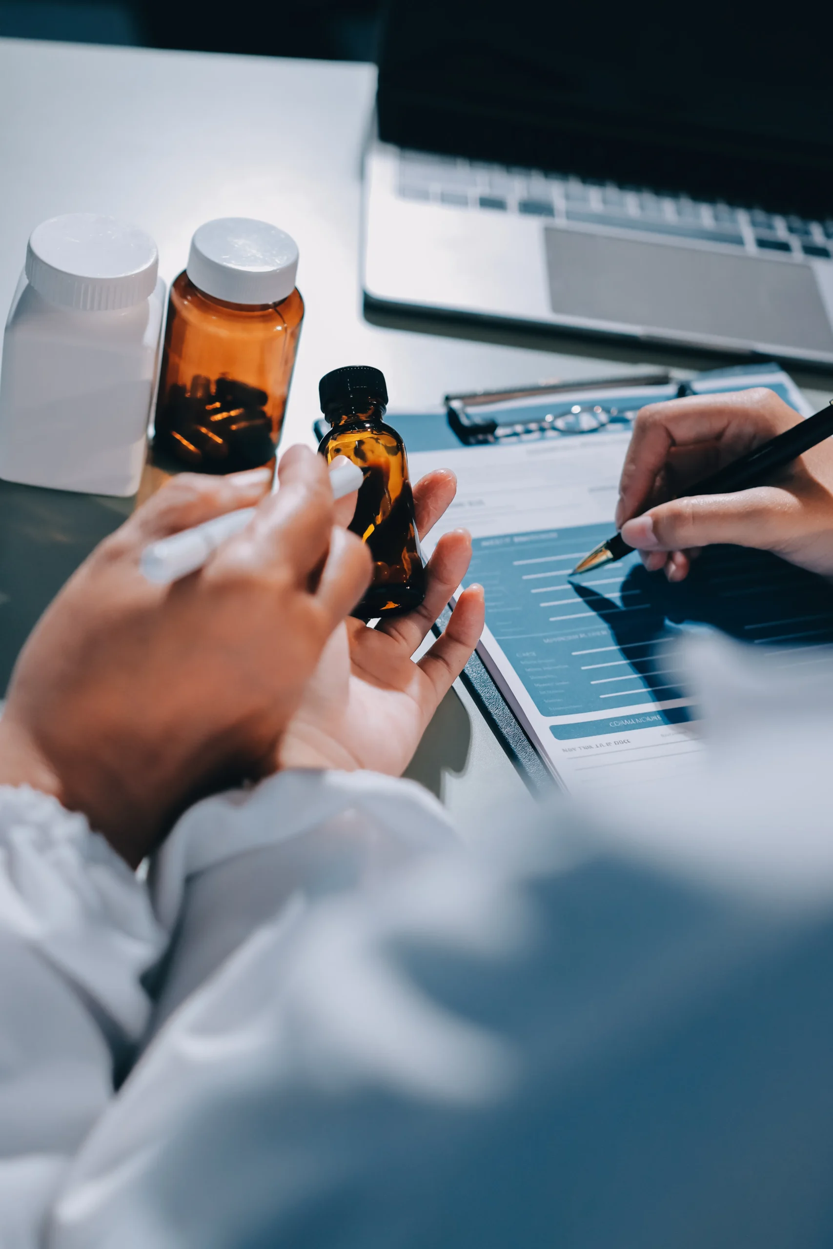 Overhead view of medical staff examining a small medicine bottle and cross-referencing information on a clipboard, utilizing a secure pharmacy drug database.