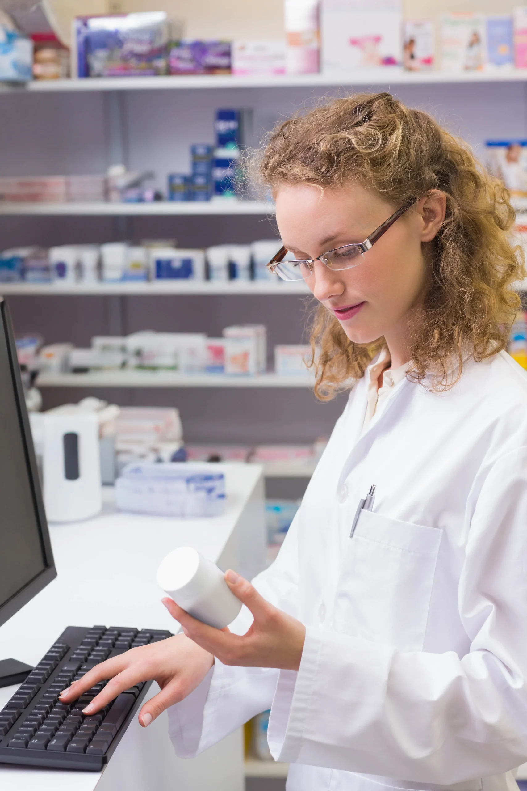 Pharmacist checking prescription details on a desktop computer using a drug interaction API.