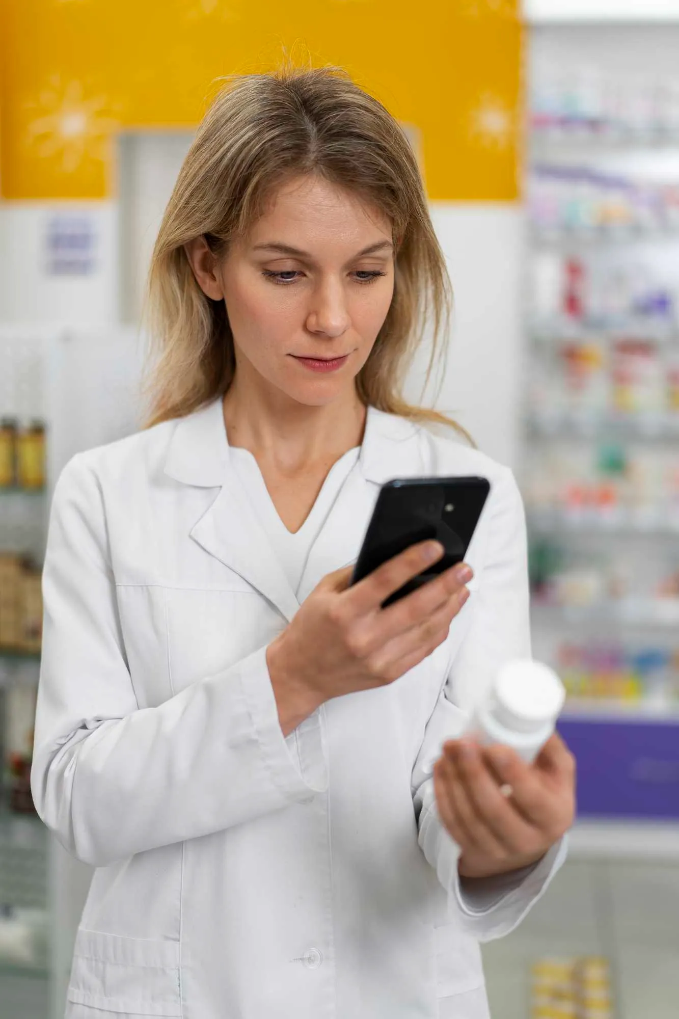 Female pharmacist scanning a medicine bottle with her smartphone, leveraging the best drug data API.