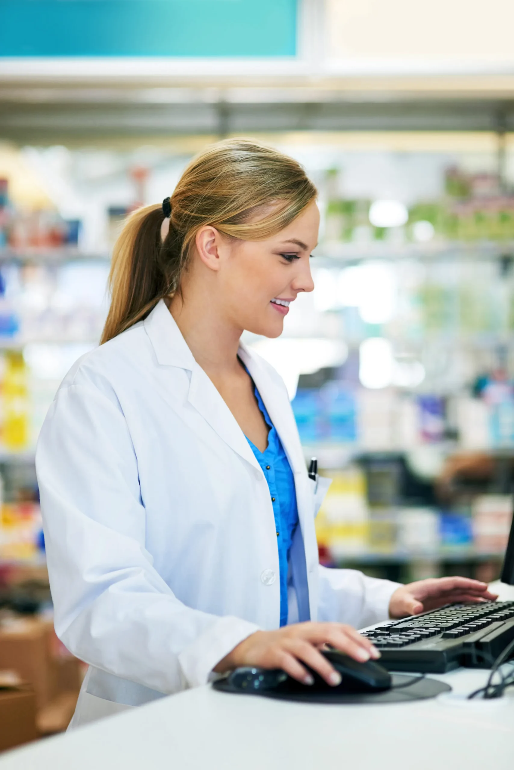 A pharmacist using a computer at a retail counter to look up medication via a drug search API.
